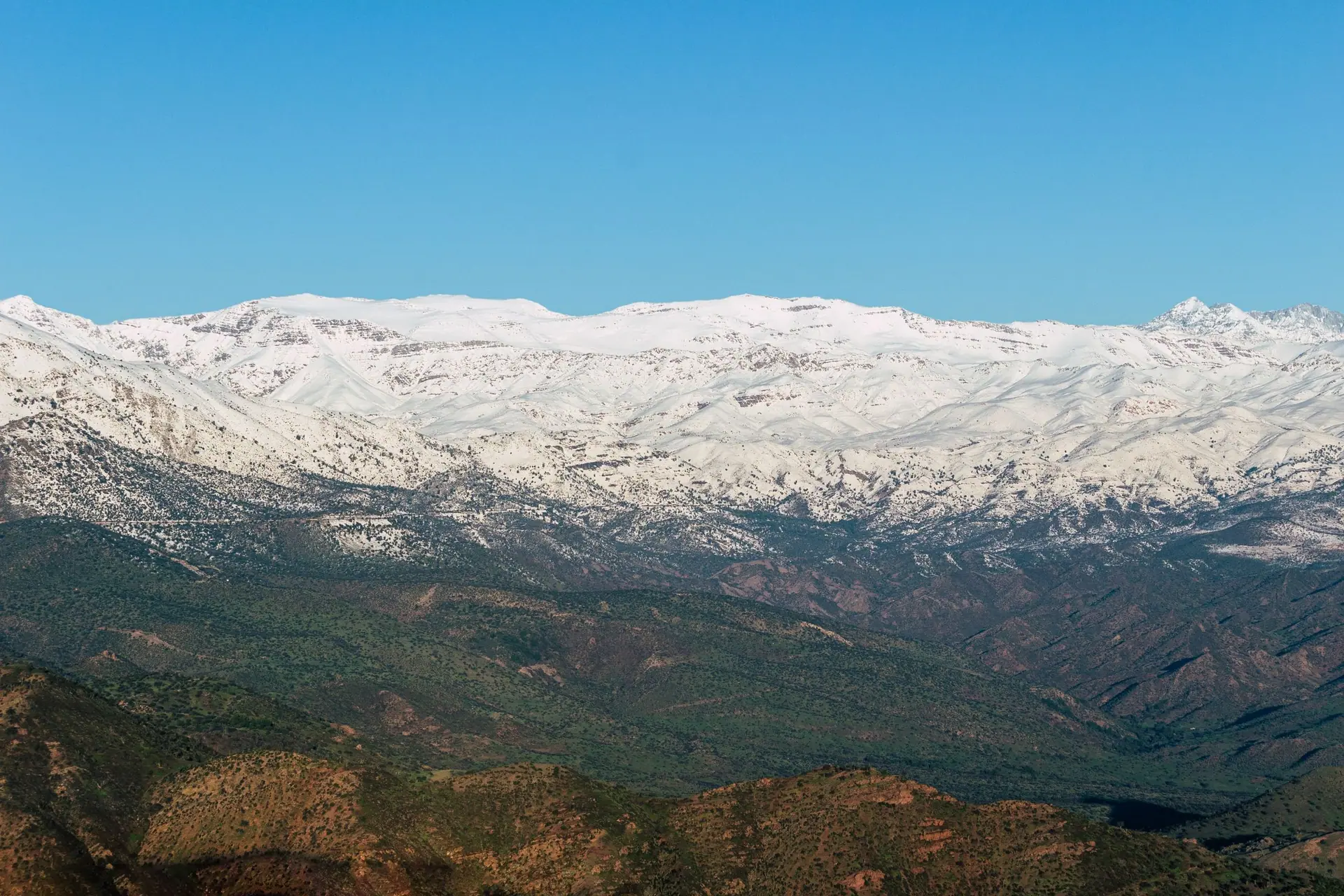 A breathtaking view of the snow-covered Atlas Mountains set against a clear blue sky, showcasing nature's beauty.