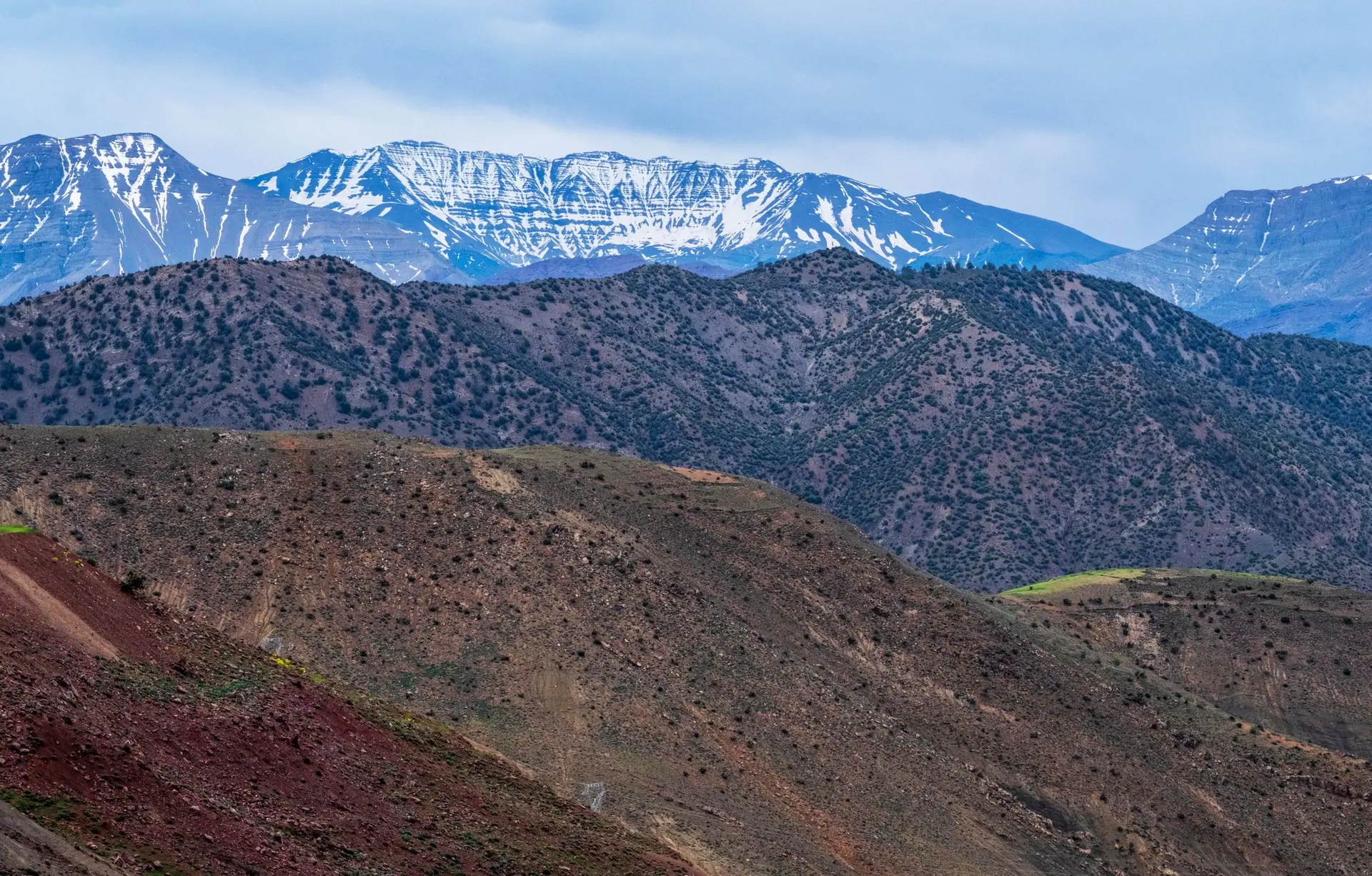 Breathtaking landscape of the Atlas Mountains with snowy peaks and arid foreground in Morocco.