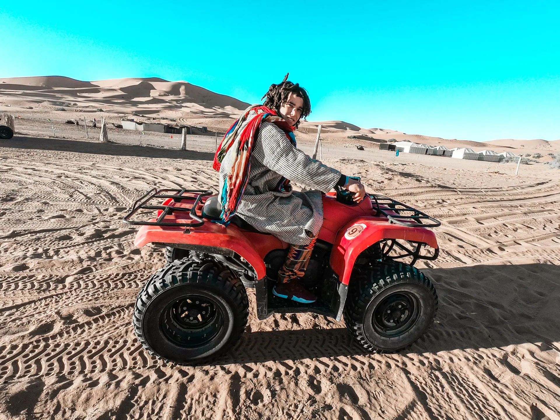 A person rides an ATV across the sandy landscape in Merzouga, Morocco.