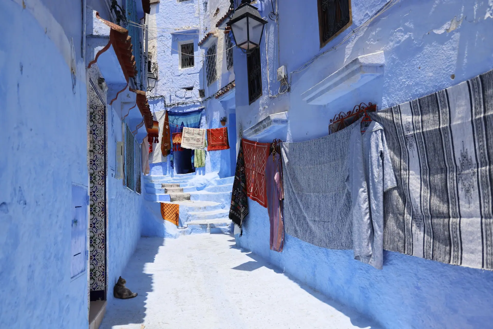 Vivid blue alleyway in Chefchaouen, Morocco with colorful drying clothes, vibrant architecture, and sunny ambiance.