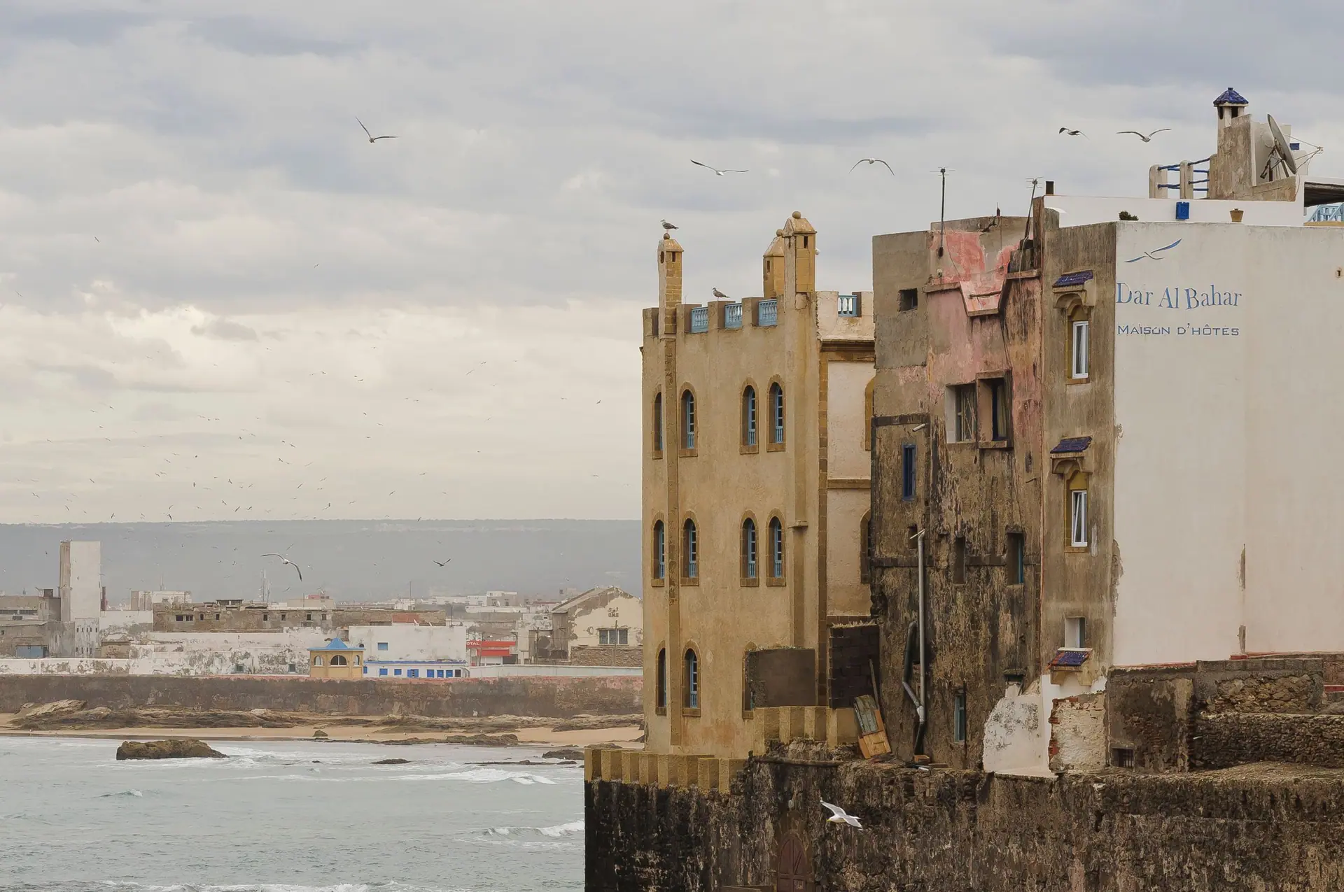 Exterior of aged shabby residential buildings located on embankment over wavy ocean against cloudy sky in Essaouira