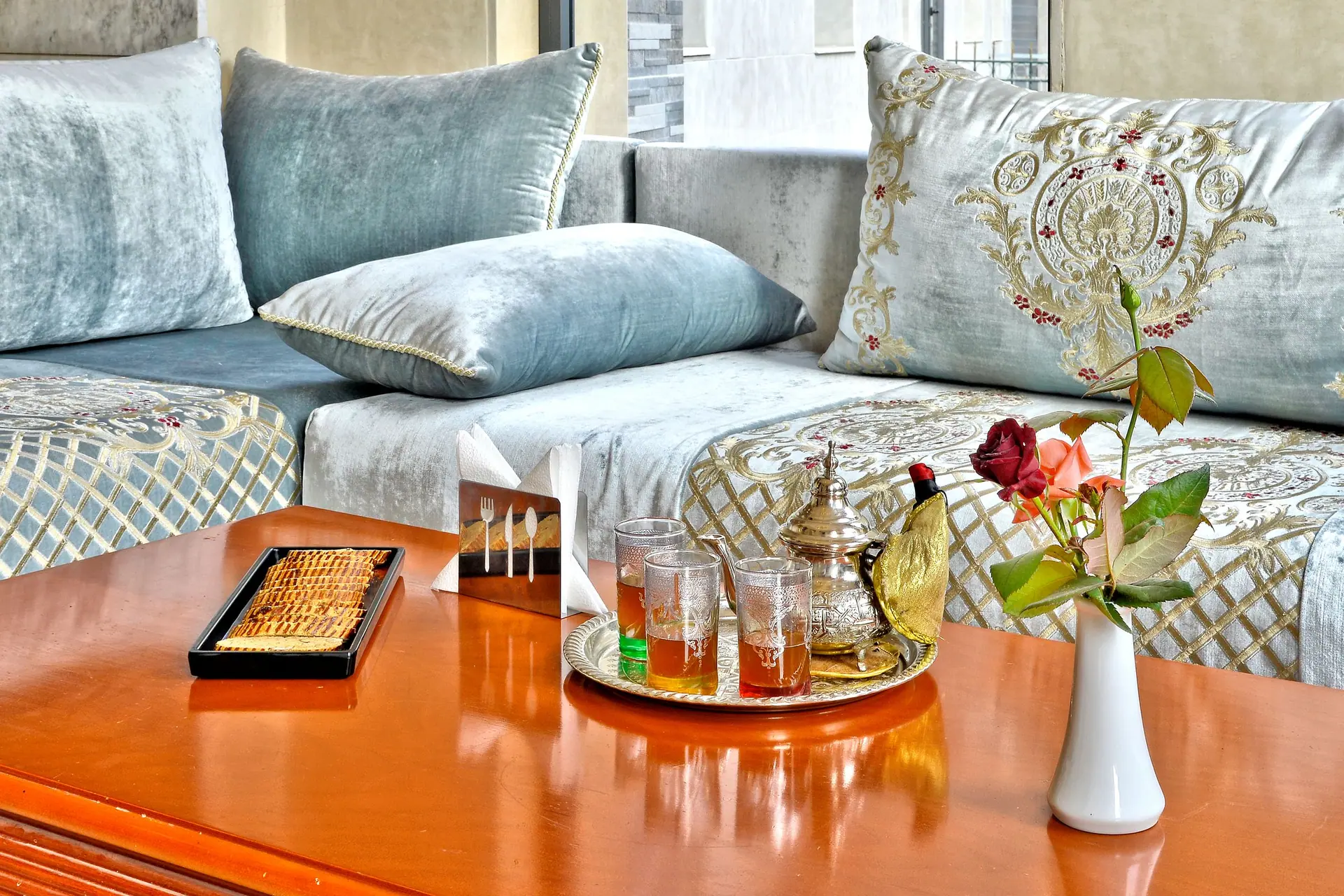 Elegant Moroccan tea setup with ornate pillows, teapot, and mint tea on a wooden table in Fès.