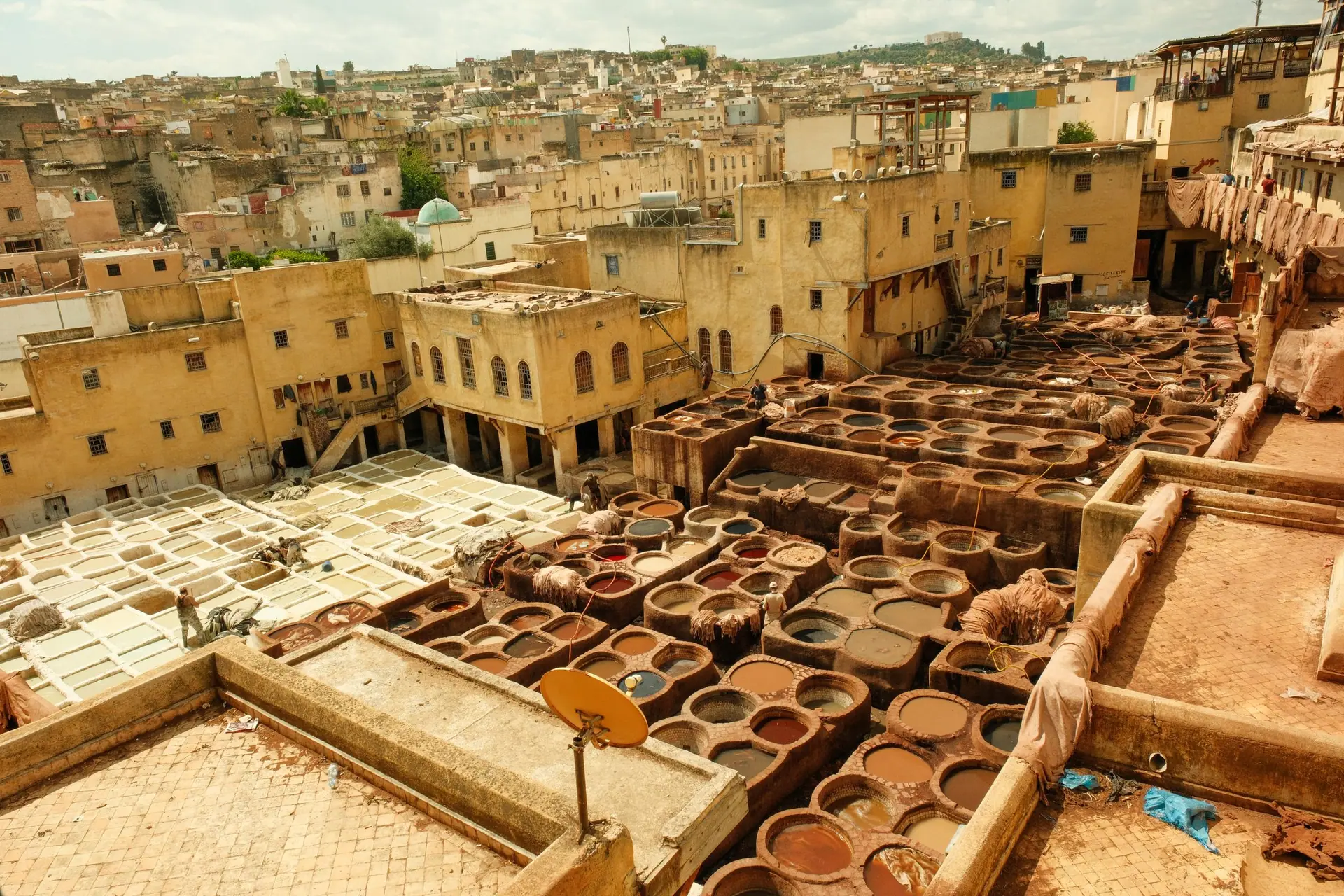 Aerial view of the vibrant traditional tannery in Fes' historic medina, showcasing colorful dye vats and architecture.